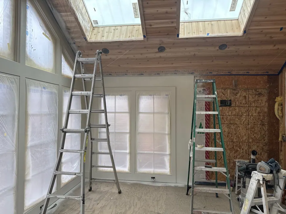 Interior painting in progress with ladders and masked windows
